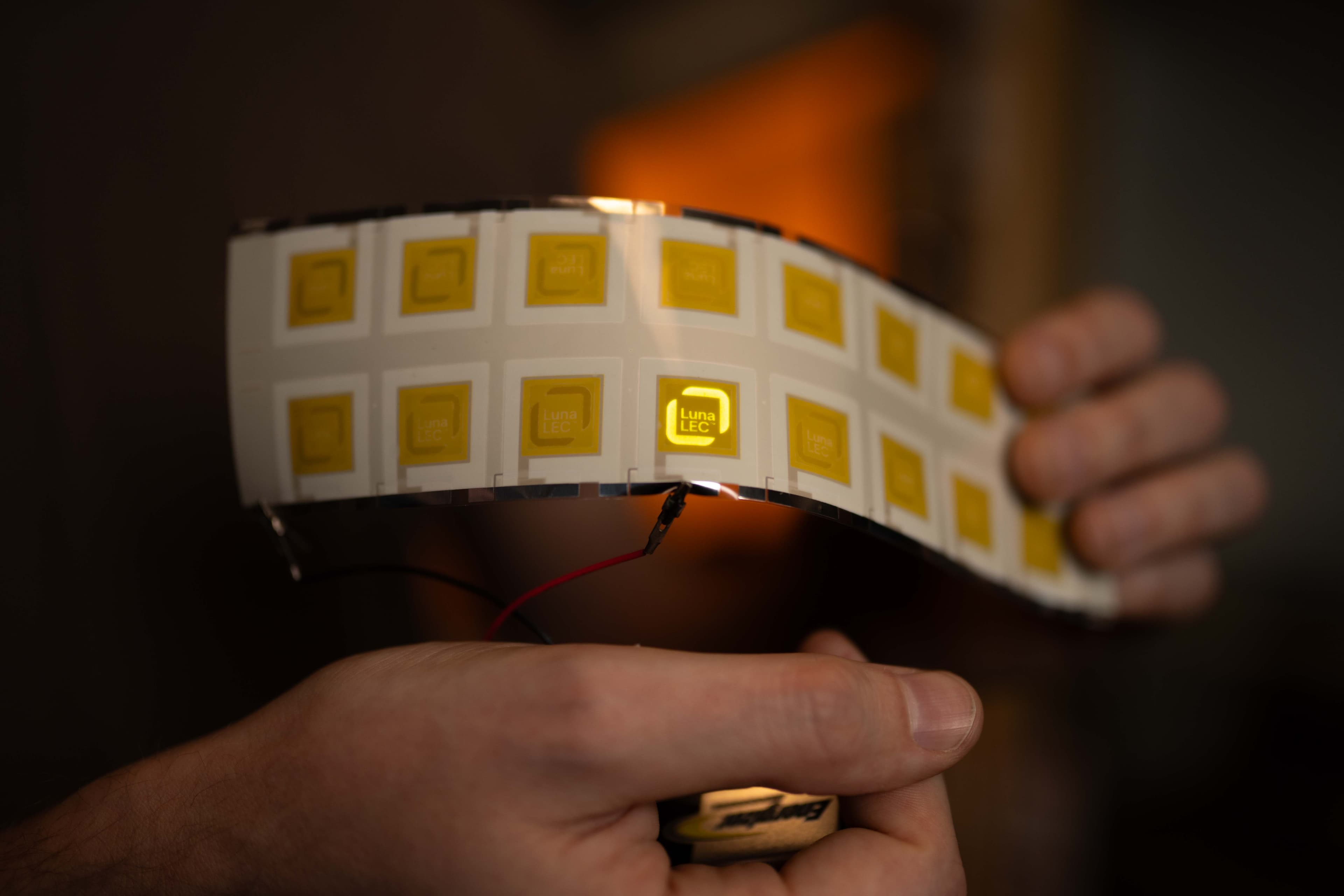 Flexible LEC tile band glowing yellow, held in hand